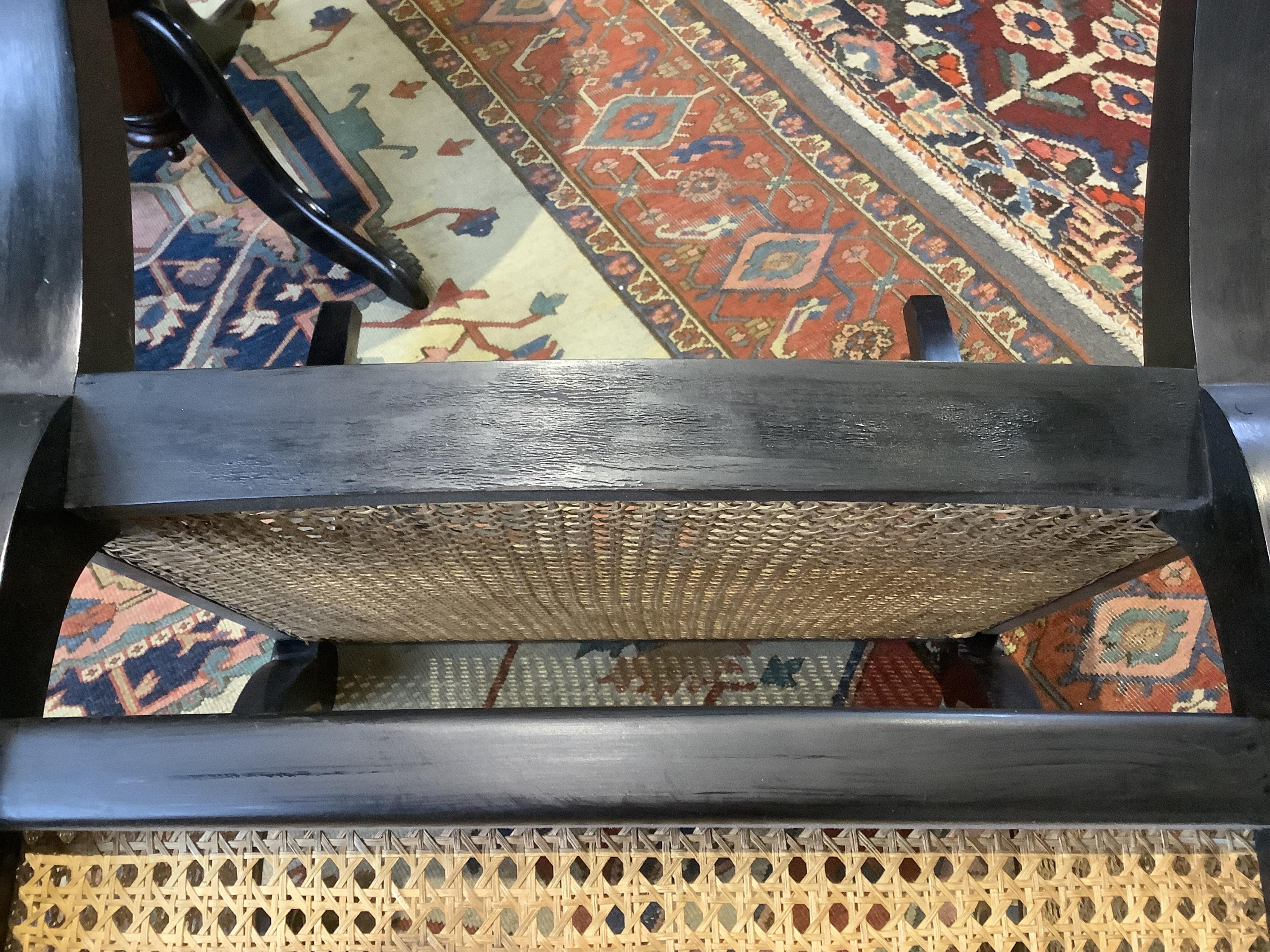 A pair of Regency style ebonised, parcel gilt caned bergere elbow chairs